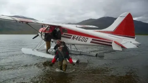 People wading beside a red and white floatplane at the shoreline