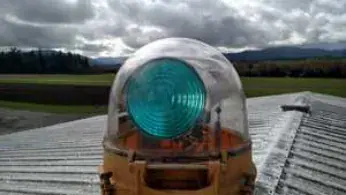A rotating airport beacon with green lens on a rooftop