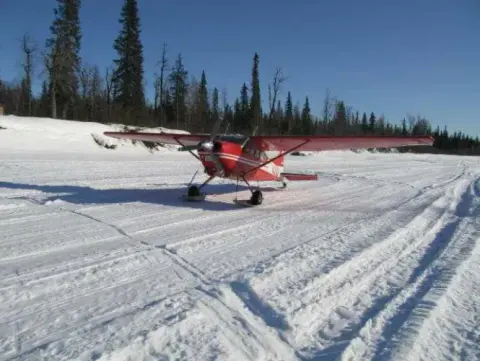 A red taildragger on a snow-covered runway lined with trees