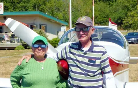 A couple standing in front of a parked low-wing airplane