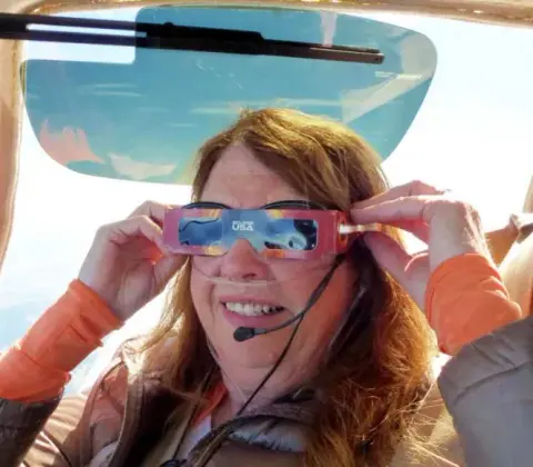A woman wearing eclipse viewing glasses under a wing