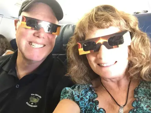 A man and a woman in the cockpit wearing eclipse glasses