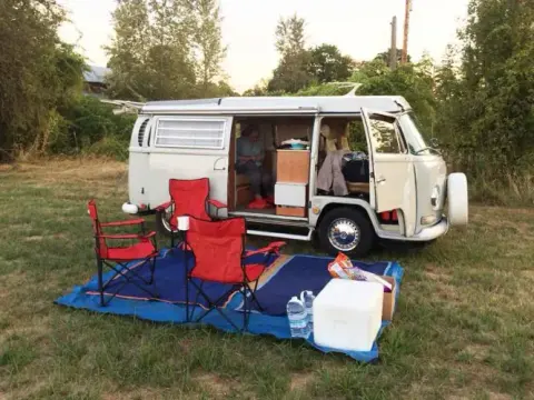 A camper van with camp chairs set up on the grass