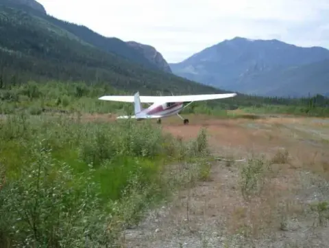 A high-wing airplane on a grass strip in a mountain valley