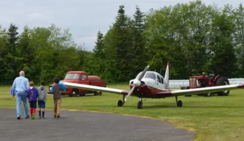 A red and white airplane taxiing with people watching nearby