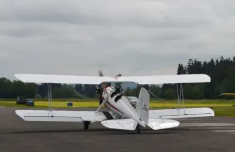 A white biplane with a cabin parked on the ramp