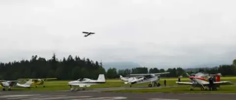 An airplane taking off over a field of parked airplanes