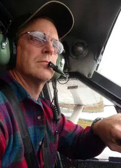 A pilot in a cap, glasses and headset at the controls in a cockpit