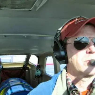 A pilot in a red cap, sunglasses and headset in a cockpit