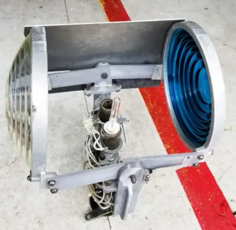 A rotating beacon fixture with blue lens on a red and white striped surface