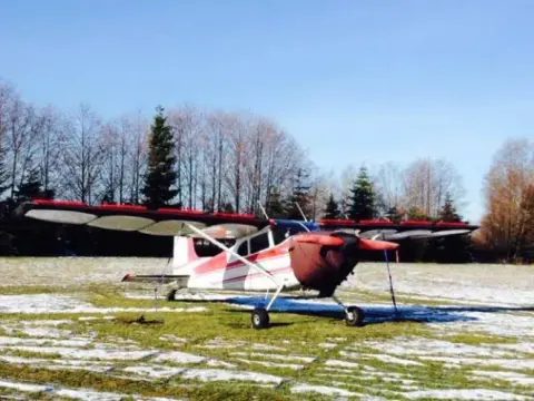 A red and white high-wing airplane parked on frosty grass