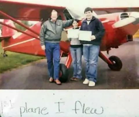 Two people holding certificates in front of a red airplane, with a handwritten note below
