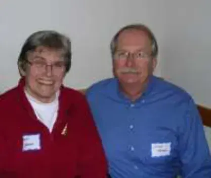 A smiling woman in a red sweater and a man in a blue shirt, both wearing name tags