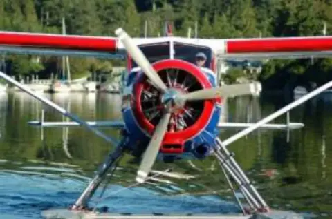 The nose and propeller of a red and white floatplane at a dock