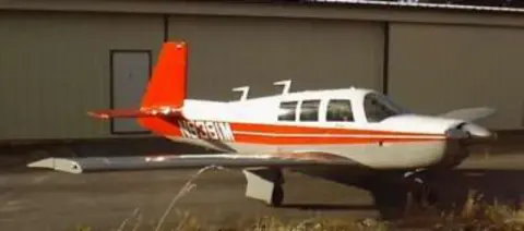 A white and orange low-wing airplane in front of a hangar
