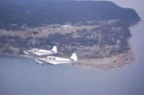 Two white airplanes flying in formation over a coastal town