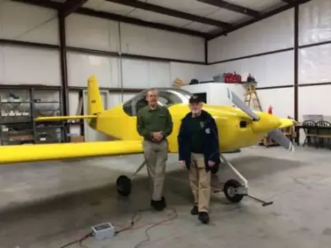 Two men standing beside a yellow RV-14 in a hangar