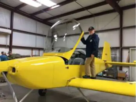 A man sitting in the cockpit of a yellow RV-14 in a hangar