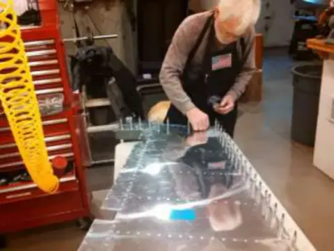 A woman drilling a metal wing part on a workbench, with a rib template hanging nearby