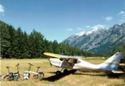 A small airplane parked in a mountain meadow with bicycles nearby