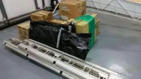 Long tube frame pieces and boxed parts on a hangar floor