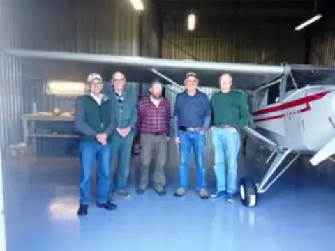 A group of men standing in front of a white airplane in a hangar