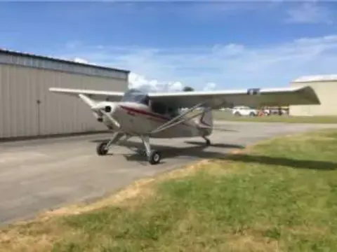 A high-wing airplane parked at the edge of a grass strip