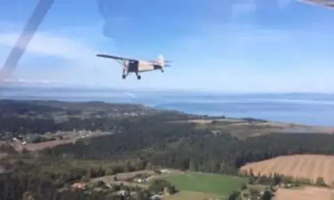 A small airplane flying over farmland and water