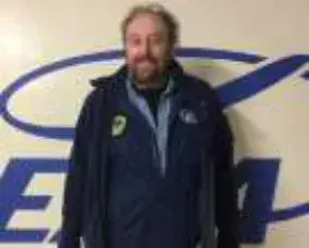 A bearded man in a navy jacket in front of an EAA logo