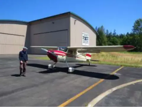 A red and white Cessna 150 parked outside a hangar