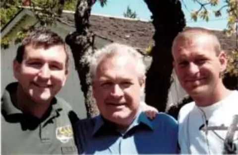 Three men smiling for a selfie outdoors