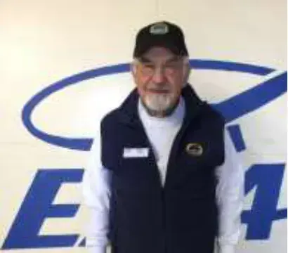 A bearded man in a black cap and vest in front of an EAA logo