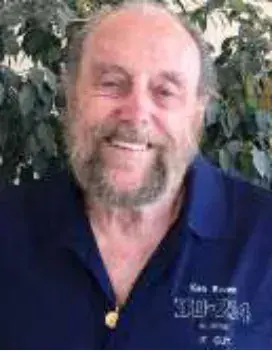 A smiling bald man with a white beard in a navy polo shirt