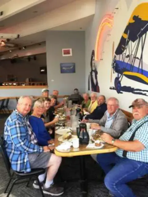Members seated at a meeting table beside an airplane wall display