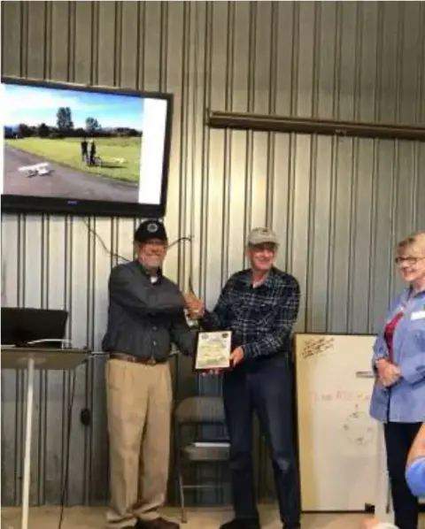 Two men presenting a framed certificate in a hangar