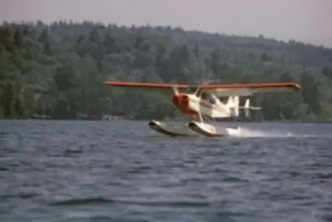 A white floatplane taking off from a lake