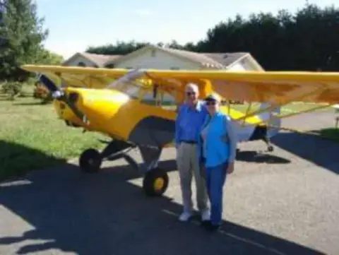 A couple standing beside a yellow airplane on a driveway