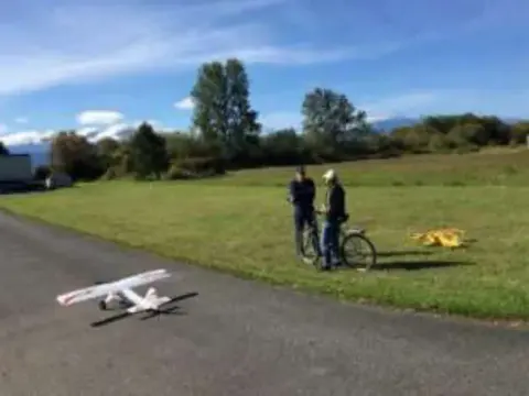 People on a grass field with a white model airplane on the pavement