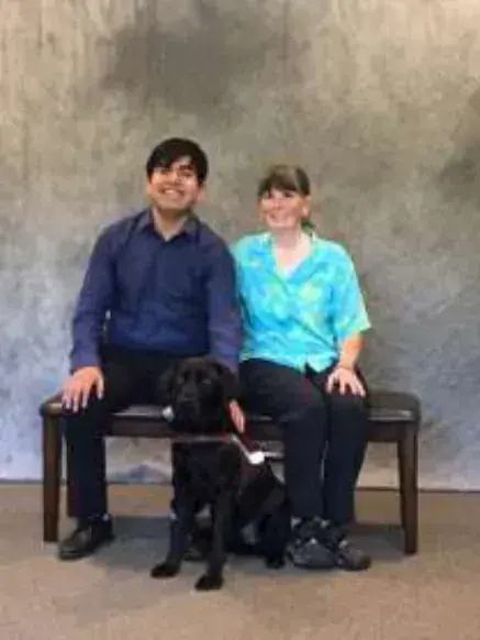 A man and a woman seated on a bench with a dog
