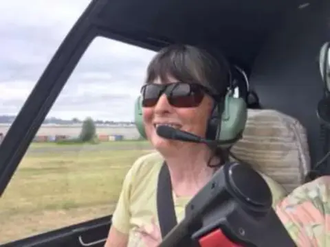 A smiling woman in sunglasses and a headset in a cockpit