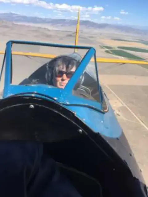 A woman in the open cockpit of a blue biplane