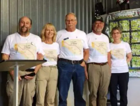 A group in matching white shirts standing in a hangar