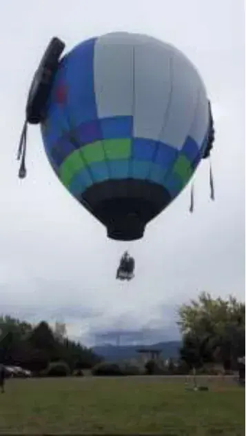 A blue and green hot air balloon rising above a field