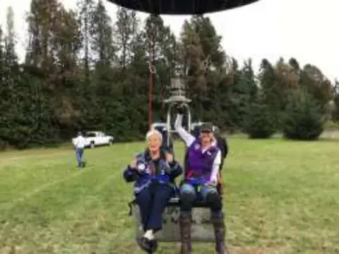Two women seated in a balloon basket on a grassy field