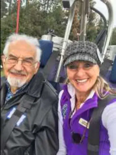 A white-bearded man and a woman in a purple vest in a balloon basket