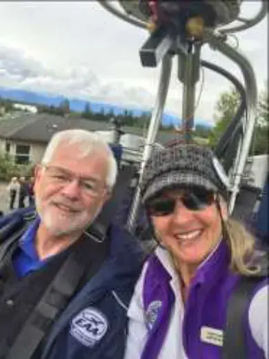 A white-haired man and a woman in a purple vest in a balloon basket