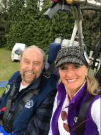 A bald man and a woman in a purple vest in a balloon basket