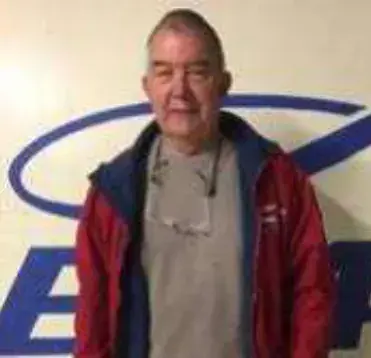 An older man in a red jacket in front of an EAA logo