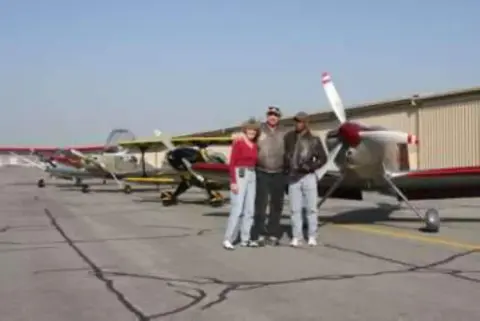 People standing next to a row of parked airplanes at a fly-in