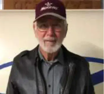 A smiling man with a white beard in a maroon cap and black jacket